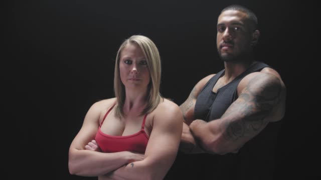 Portrait-shot-of-an-athletic-man-and-woman-crossing-their-arms-on-a-dark-background