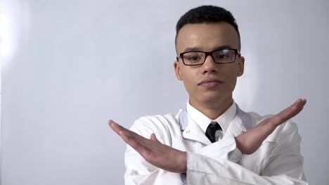 Young-successful-African-scientist-in-a-white-coat-and-glasses-showing-stop-sign,-no,-never-gesture,-crossed-his-arms,-looking-at-the-camera,-portrait-concept.-60-fps