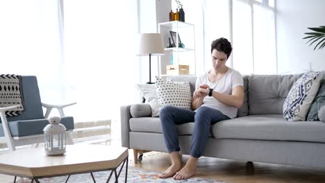 Junge-Mann-mittels-Smartwatch-während-der-Entspannung-auf-Sofa