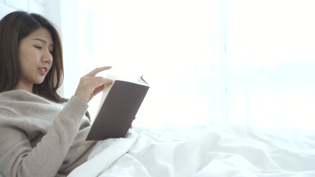 Lifestyle-happy-young-Asian-woman-enjoying-lying-on-the-bed-reading-book-pleasure-in-casual-clothing-at-home.-Relaxing-lifestyle-woman-concept.