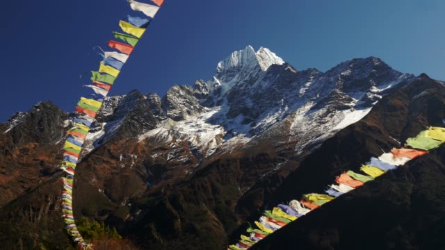 Multi-colored-Buddhist-flags-ripple-in-the-wind-against-the-background-of-snow-capped-mountains