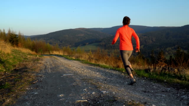 Junge-sportliche-Frau-läuft-im-Freien-bei-Sonnenuntergang-in-Berglandschaft.