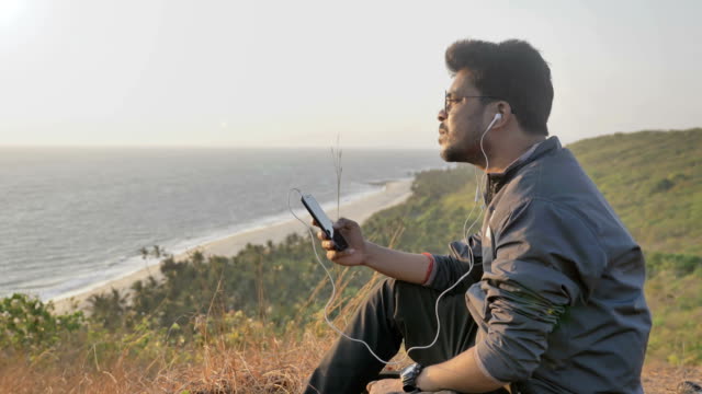 Un-joven-sentado-sobre-una-colina-viendo-y-escuchando-música-y-disfrutando-de-una-vista