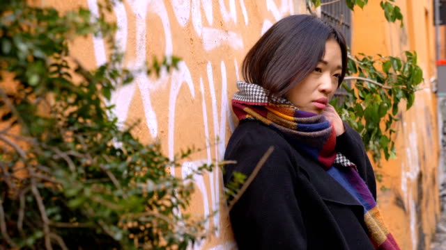 Mujer-asiática-sola-triste-y-pensativa-apoyado-contra-una-pared-en-la-calle