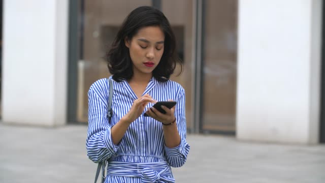 Mujer-asiática-joven-usando-el-teléfono-inteligente-en-la-calle