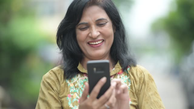 Madura-feliz-bella-mujer-India-con-teléfono-en-las-calles-al-aire-libre