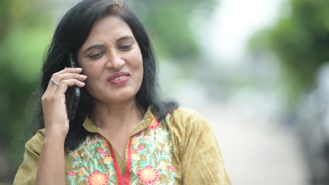Madura-mujer-India-hermosa-feliz-hablando-por-teléfono-mientras-pensaba-en-el-exterior-de-las-calles
