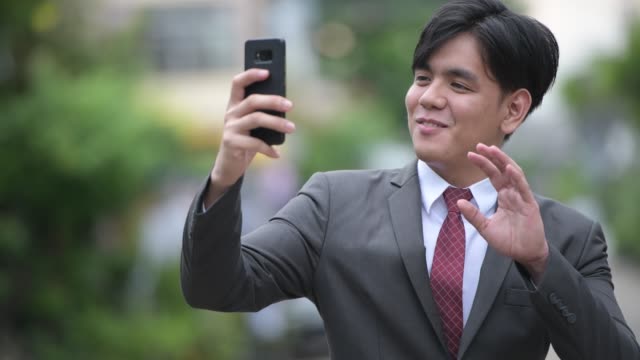 Young-handsome-Asian-businessman-using-phone-in-the-streets-outdoors
