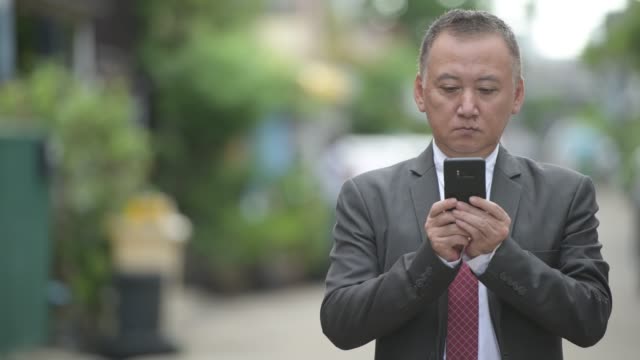 Mature-Japanese-businessman-using-phone-in-the-streets-outdoors