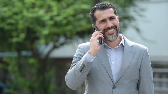 Handsome-Persian-bearded-businessman-talking-on-phone-in-the-streets-outdoors