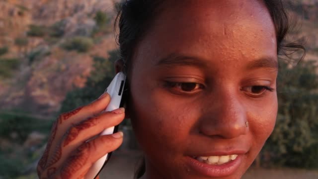 Teenage-girl-dials-talks-idea-smart-mobile-phone-looking-around-outdoor-nature-hill-top-smile-happy-joy-fun-panoramic-view-viewpoint-sunset-dusk-on-a-hot-summer-day-in-India-handheld-stabilized-sand