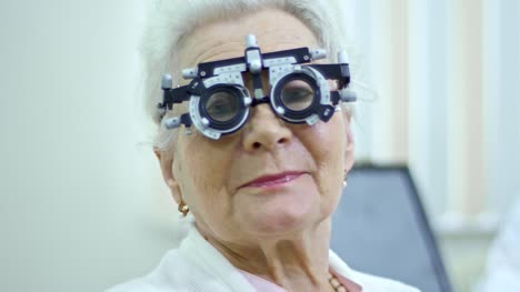 Senior-mujer-posando-en-el-marco-de-prueba-en-clínica-de-atención-oftalmológica