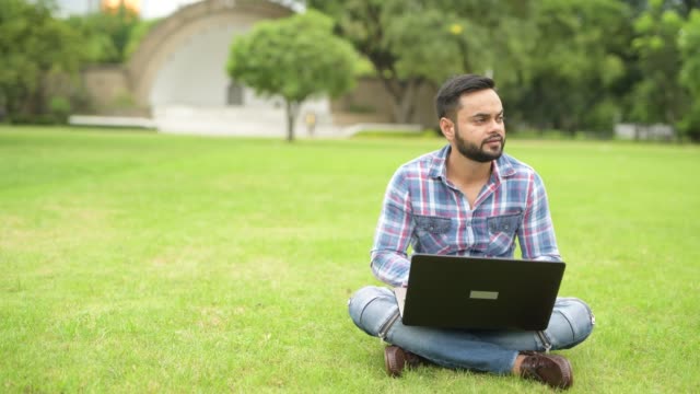 Joven-guapo-indio-en-el-parque-con-ordenador-portátil
