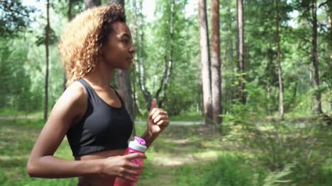 young-beautiful-African-American-woman-with-curly-hair-running-with-pink-bottle-in-a-forest
