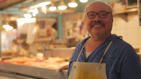 A-hispanic-man-with-a-mustache-butcher-standing-in-front-of-a-fish-market