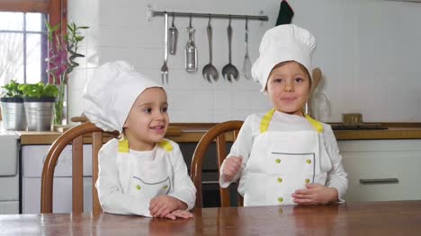 Portrait-of-two-sisters-in-the-kitchen-dressed-as-professional-chefs-who-smile-and-kisses-looking-at-the-camera-with-their-arms-folded-by-real-professional-chefs.