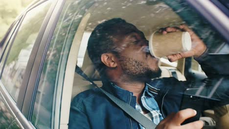 Handsome-Black-Man-Traveling-in-a-Car,-Sitting-on-a-Passenger-Seat-Uses-Smartphone,-Drinks-Coffee.-Camera-Shot-from-Outside-the-Vehicle.