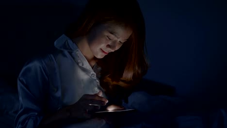 Hermosa-mujer-asiática-en-ropa-de-noche-está-usando-el-teléfono-inteligente-en-la-cama-en-el-antes-de-dormir-por-la-noche.