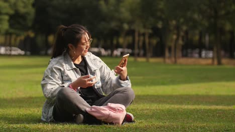 Asiatische-College-Mädchen-sitzen-auf-dem-Rasen-mit-Handy-auf-dem-campus