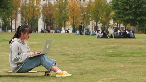 Asian-college-girl-sitting-on-skateboard-using-laptop-in-campus