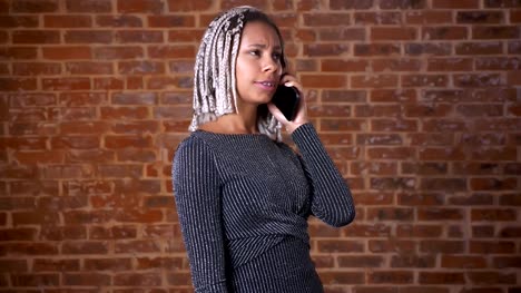 Chica-africana-joven-con-rastas,-hablar-por-teléfono,-pared-de-ladrillos-en-el-fondo.