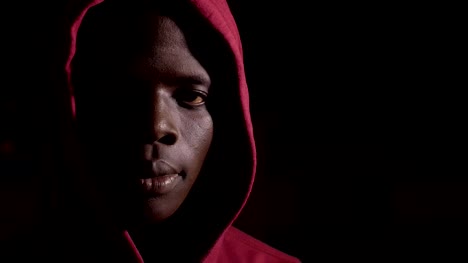 Hombre-africano-negro-joven-encapuchado-en-la-oscuridad-mirando-a-cámara