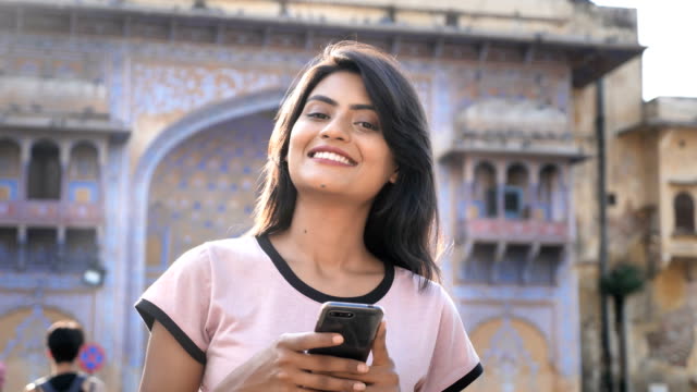 n-attractive-girl-smiling-looking-at-the-camera-on-a-city-street-holding-smartphone