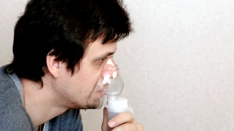 Utilice-el-nebulizador-y-el-inhalador-para-el-tratamiento.-Hombre-joven-inhalando-a-través-de-la-tos-y-la-máscara-de-inhalador.-Vista-lateral.