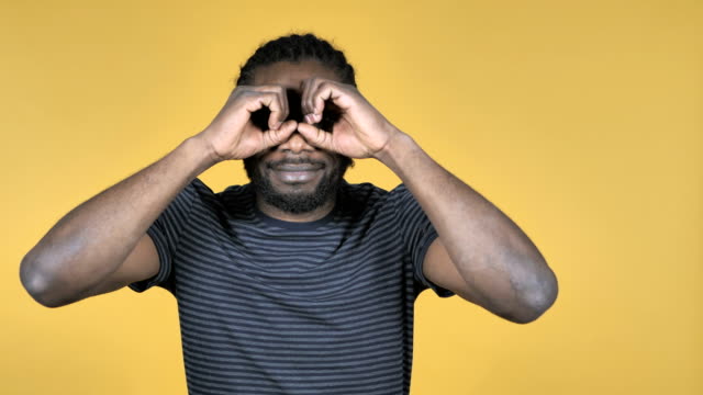 Casual-hombre-africano-buscar-con-binoculares-a-mano-aisladas-sobre-fondo-amarillo