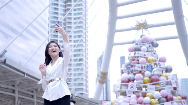Junge-asiatische-Geschäftsfrau-mittels-Smartphone-nehmen-Selfie,-glücklich-lächelnd-im-Stadtzentrum-von-Bangkok,-Thailand.-täglichen-Lebens-Technologiekonzept.-SLOW-MOTION