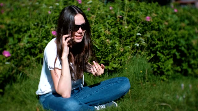 Beautiful-young-woman-is-calling-and-talking-on-mobile-phone-sitting-in-the-park.