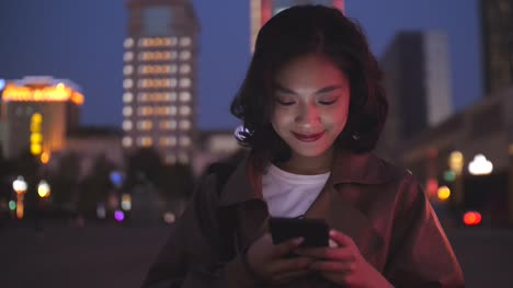 pretty-young-asian-woman-using-mobile-phone-in-the-city-street-at-night,-4k