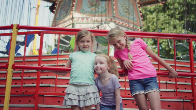 Three-little-girls-smiling-in-front-of-a-carnival-ride