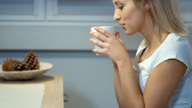 Cheerful-young-woman-holding-mug-in-the-kitchen-at-home.