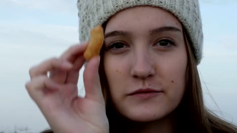 Retrato-de-una-adolescente-en-una-gorra-de-punto,-que-muestra-y-comiendo-botanas-maní-israelies-Bamba,-al-aire-libre,-stock-de-metraje.