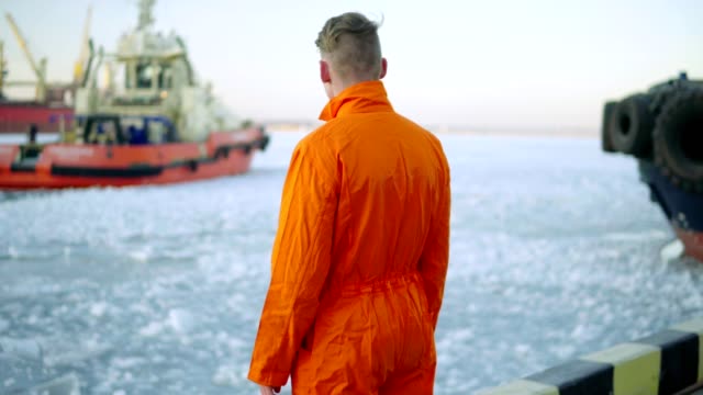 Dock-Arbeiter-in-orange-Uniform-mit-Blick-auf-das-Meer-und-Wandern-in-den-Hafen-im-Winter.-Vereisten-See