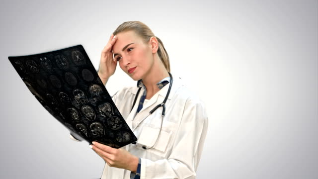 Ärztin,-ernsthaft-betrachtet-Xray-Ergebnisse-des-menschlichen-Gehirns-auf-weißem-Hintergrund