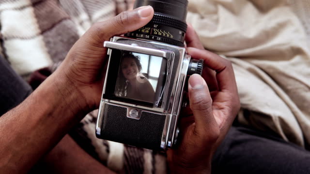 Close-up-view-of-african-man-holding-old-photocamera,-taking-photo-portrait-beautiful-woman.-Multiracial-couple-on-bed