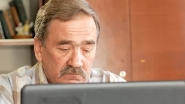Ein-älterer-Mann-mit-einem-Schnurrbart-sitzt-hinter-einem-Laptop-und-löst-Probleme.-Er-schaut-ernst-auf-dem-monitor