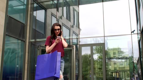 Young-girl-with-phone-and-shopping-bags-near-Mall.