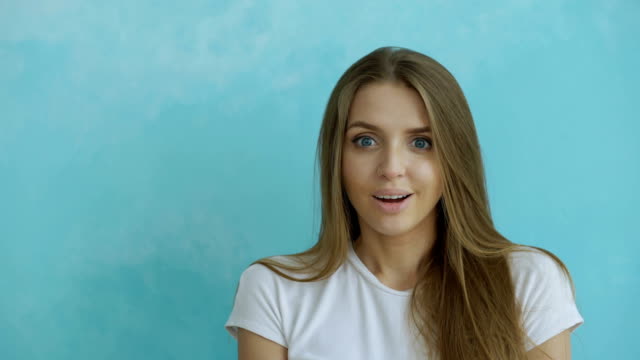 Portrait-of-young-woman-actively-surprising-and-wondering-looking-into-camera-on-blue-background