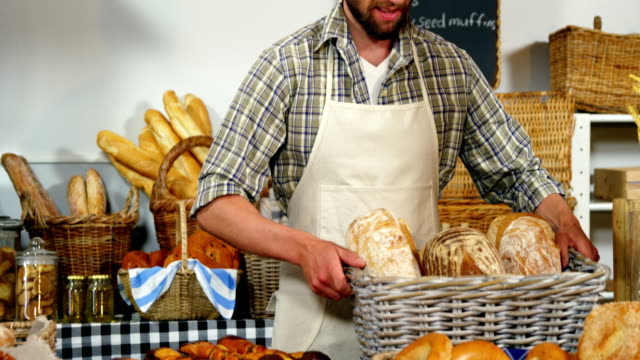 Portrait-of-male-staff-holding-breads-in-basket-at-bakery-section