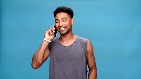 Young-smiling-african-man-talking-by-phone-over-blue-background.