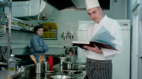 Jefe-de-cocina-busca-una-receta-en-el-libro-de-aprendiz-de-cocinero-preparar