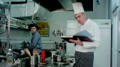 Head-chef-looking-for-recipe-in-a-book-while-checking-upon-his-cook-trainee