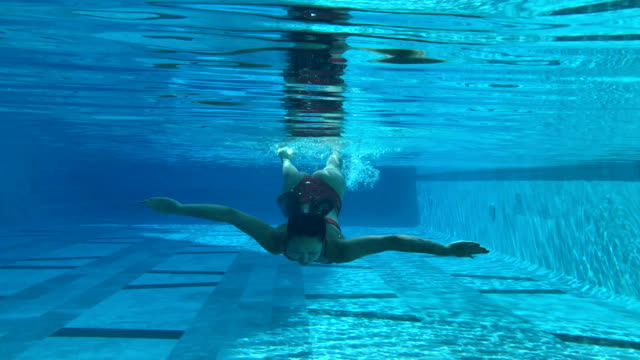 Frau-in-einem-blauen-Pool-unter-Wasser-schwimmen