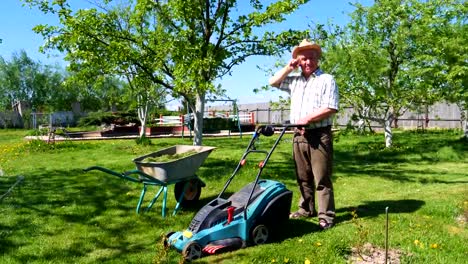 An-old-man-is-standing-with-a-lawn-mower-in-a-beautiful-garden.