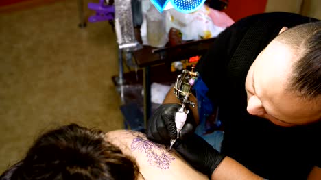 in-einem-Tattoo-Salon-ist-Spezialist-für-ein-Tattoo-auf-dem-Rücken-der-Frau,-ein-florales-Ornament-tun.-ein-Mann-arbeitet-in-spezielle-Handschuhe-auf-spezielle-Ausrüstung.-Zeichnung-erfolgt-mit-schwarzer-Farbe