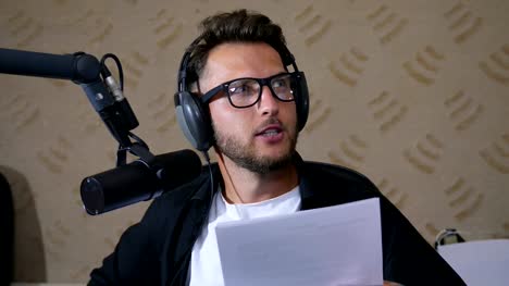 recording-studio,-close-up-young-man-in-glasses-reads-the-text-into-microphone-while-working-on-radio