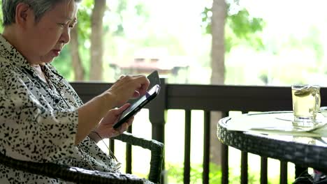 elder-Asiatin-halten-Handys-sitzend-auf-Stuhl-im-Restaurant.-ältere-Frauen-SMS-Nachricht-über-app-mit-dem-Handy-im-Park.-Senior-Verwendung-Smartphone-mit-Menschen-in-sozialen-Netzwerk-mit-Wireless-Internet-Verbindung-im-freien-verbinden.